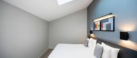 Une chambre moderne avec une lucarne, un grand lit et des luminaires fixés au mur.