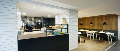 A modern cafe with a counter displaying pastries and beverages, wooden tables and chairs, and a mix of white and wooden wall panels.