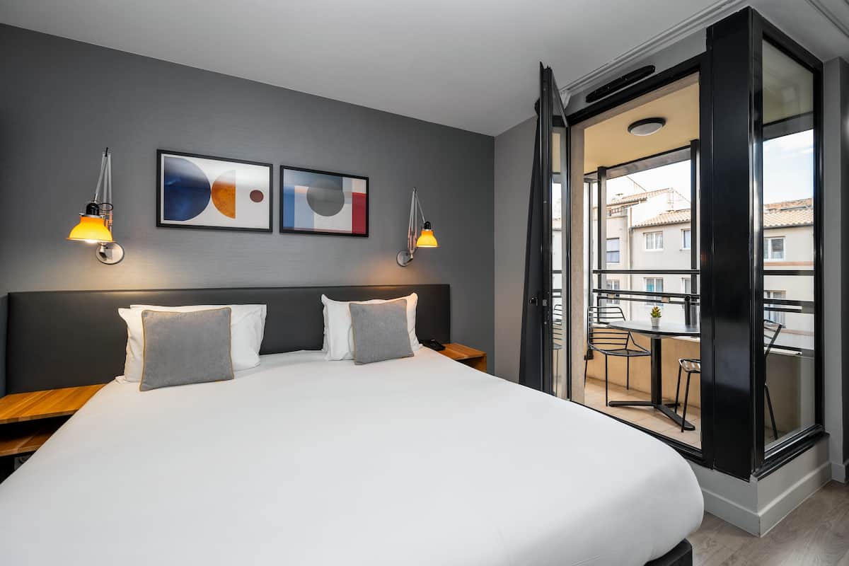 Une chambre d’hôtel moderne dotée d’un grand lit, de deux tables de chevet, d’une petite table et d’un balcon avec une table et des chaises.