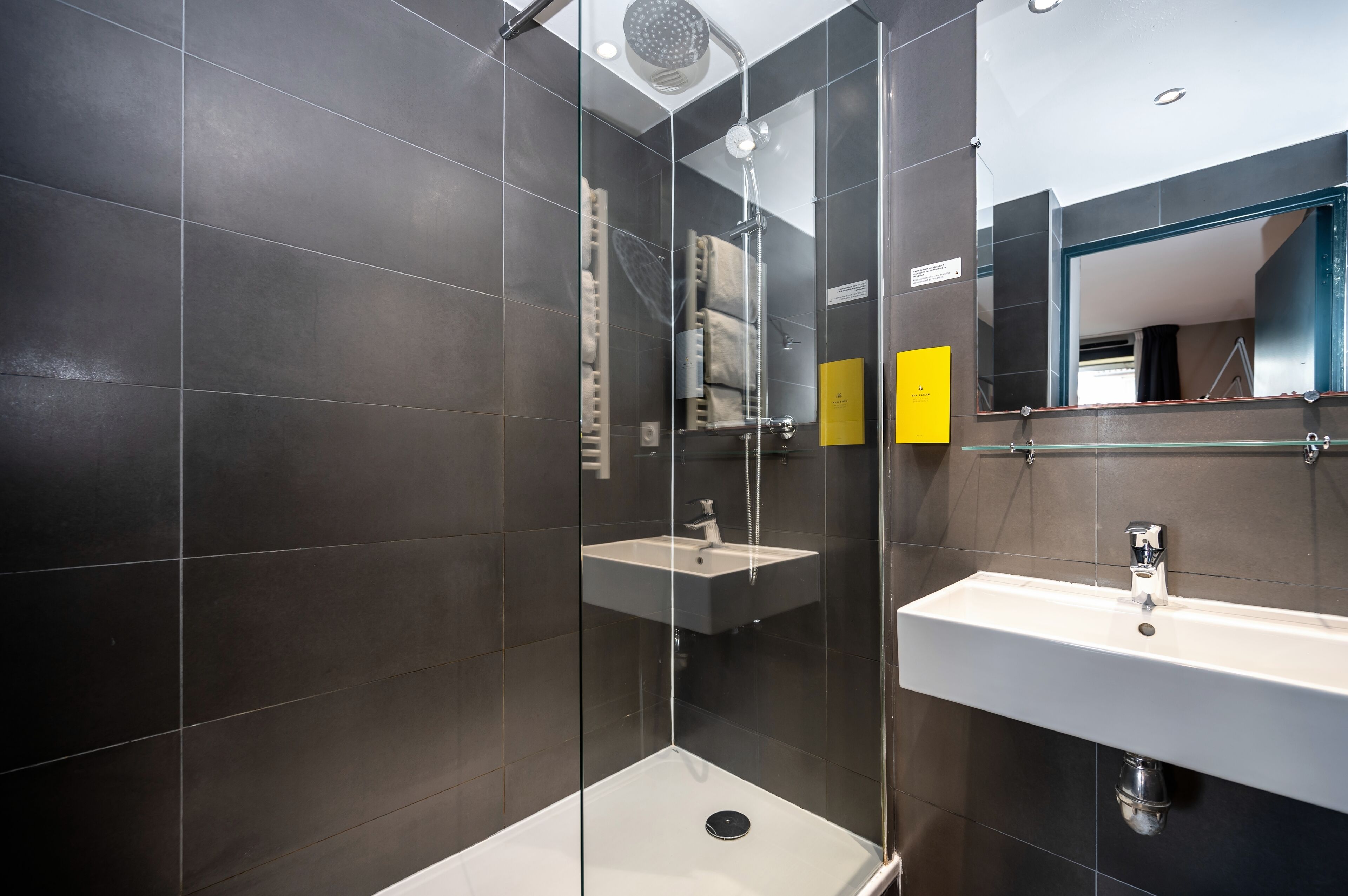 A modern bathroom with a glass-enclosed shower, a white sink, and dark tiled walls.