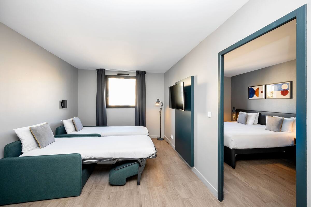 Une chambre d’hôtel moderne, équipée de deux lits, d’un bureau, d’une télévision à écran plat et agrémentée d’œuvres d’art au mur.