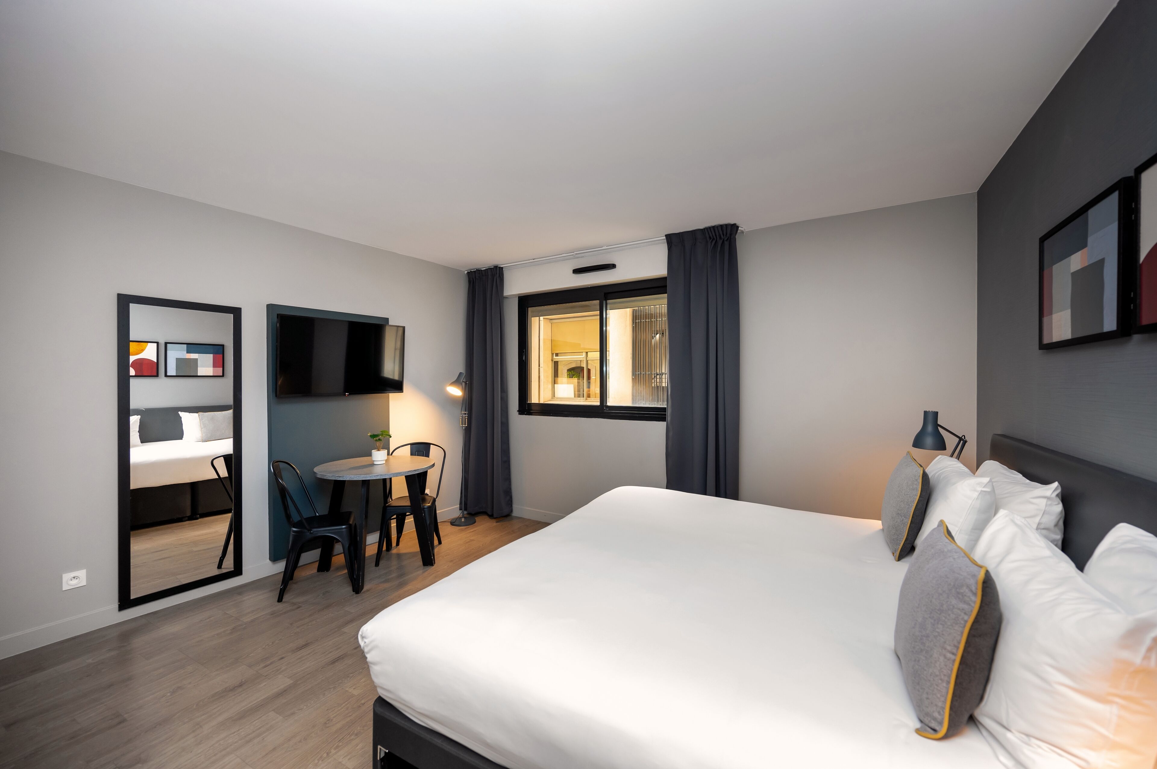 Een hotelkamer met een bed, een bureau en een stoel. Er is een raam met gordijnen, een flatscreen-televisie aan de muur en een deur naar de badkamer.