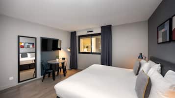Een hotelkamer met een bed, een bureau en een stoel. Er is een raam met gordijnen, een flatscreen-televisie aan de muur en een deur naar de badkamer.