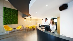 Un espace d’accueil moderne avec un comptoir incurvé, un mur végétal et des chaises jaunes.