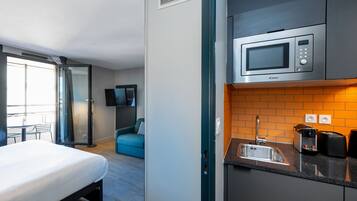 A compact hotel room with a bed, a kitchenette with a microwave, a sink, and a small dining area with a table and chairs.