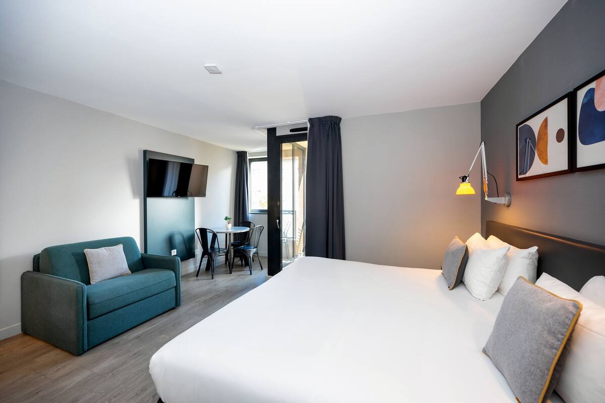 Une chambre d’hôtel moderne, dotée d’un grand lit, d’un canapé, d’une petite table et d’un téléviseur fixé au mur.