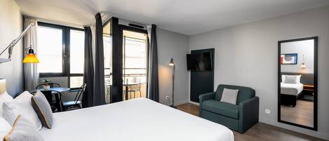 Una habitación de hotel moderna con una cama grande, un escritorio con silla, un sofá, un televisor y un balcón con cortinas.