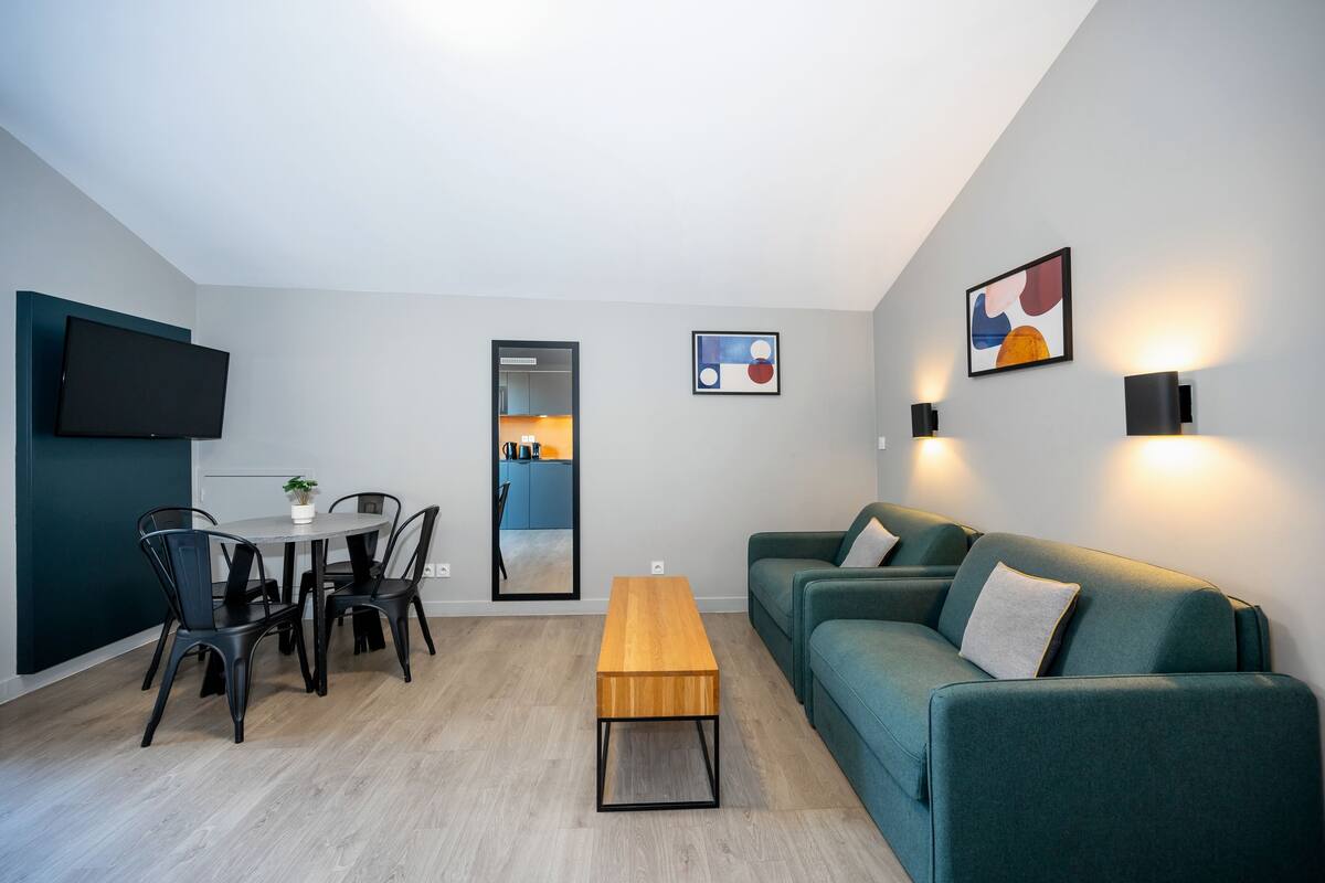 Un salon moderne avec un canapé vert, une table basse en bois et un coin repas comprenant des chaises et un téléviseur.