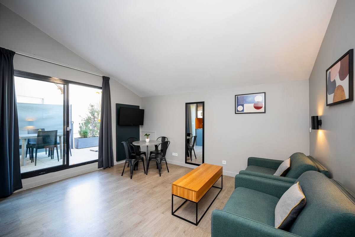 Un salon moderne comprenant un canapé, un banc en bois, une table à manger avec des chaises et une grande porte-fenêtre coulissante donnant sur un espace extérieur.