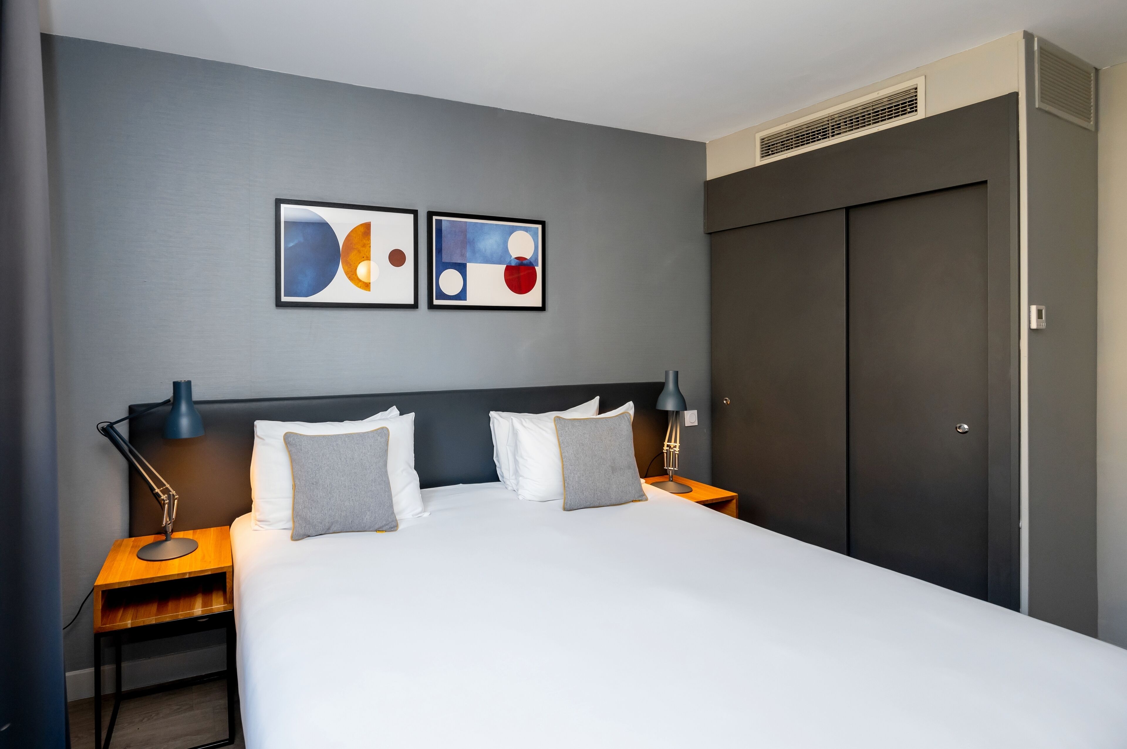 Ein modernes Hotelzimmer mit einem großen Bett, zwei Nachttischen, einem dunklen Kopfteil und abstrakter Wandkunst.