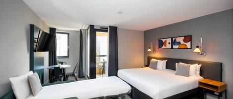 A modern hotel room with two beds, a desk, and a view of the outdoor area.