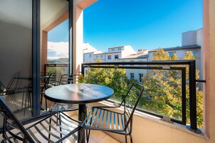 A balcony with a round table and chairs, overlooking a cityscape with buildings and trees.