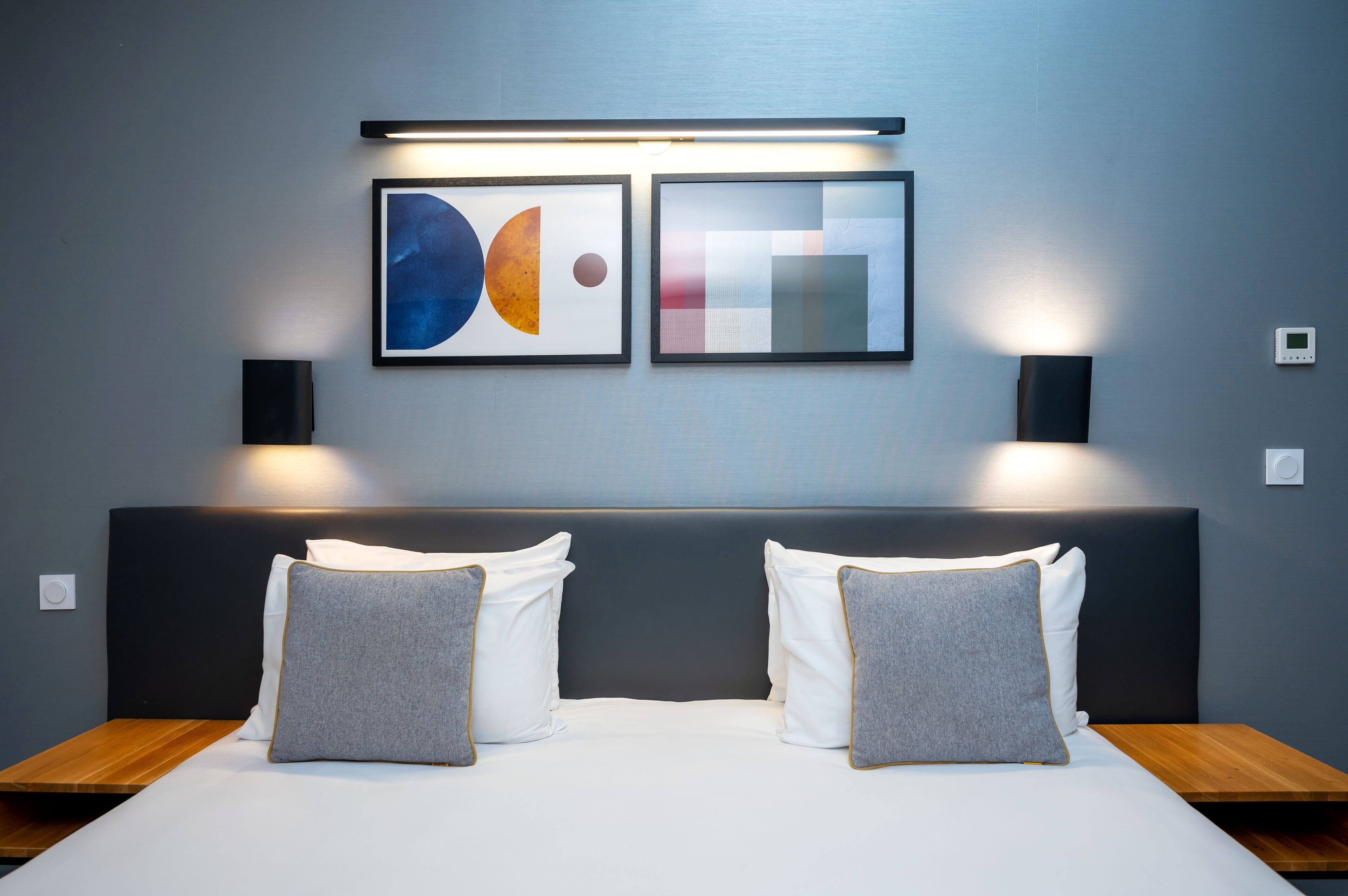 Ein modernes Hotelzimmer mit einem großen Bett, zwei Nachttischen und abstrakter Kunst an der Wand.