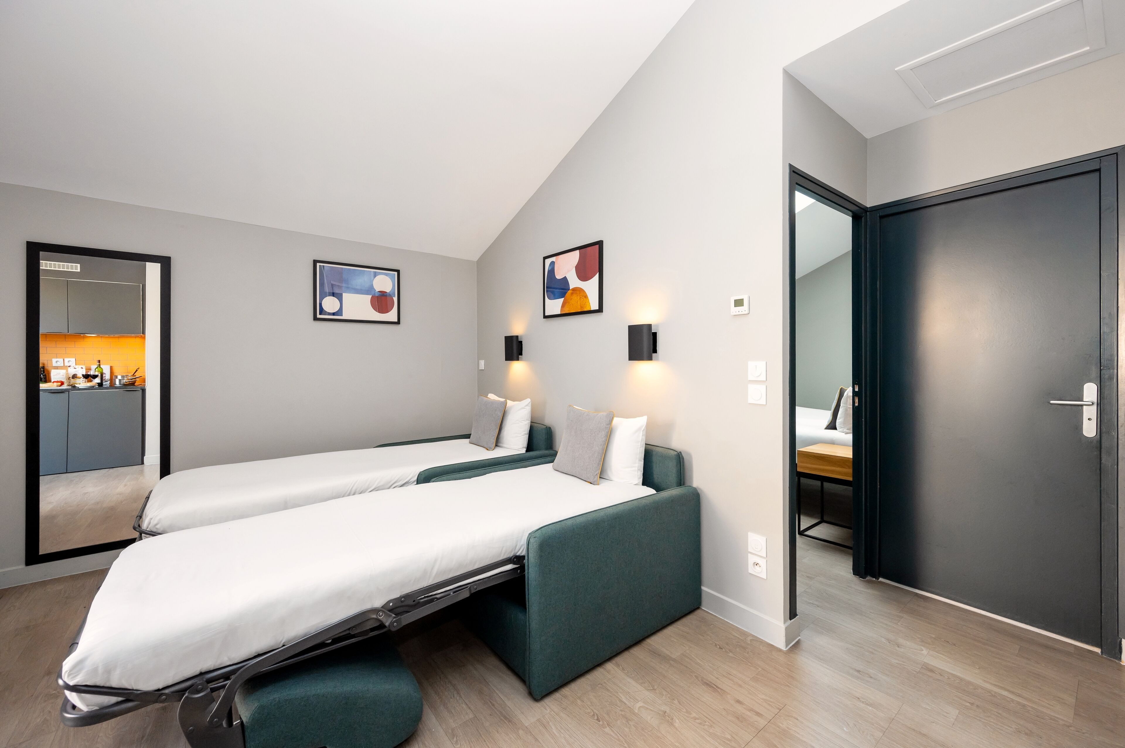 Ein modernes Zimmer mit zwei Einzelbetten, einer kleinen Küchenzeile und einer Tür zum Badezimmer.