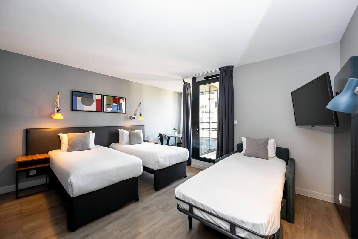 Une chambre d’hôtel moderne équipée de deux lits, d’un téléviseur  à écran plat et agrémentée d’œuvres d’art au mur.