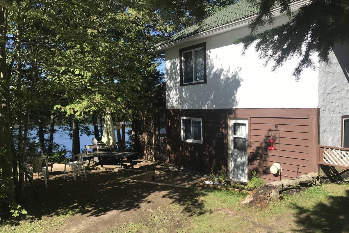 A two-story house with a dock extending into a body of water, surrounded by trees.