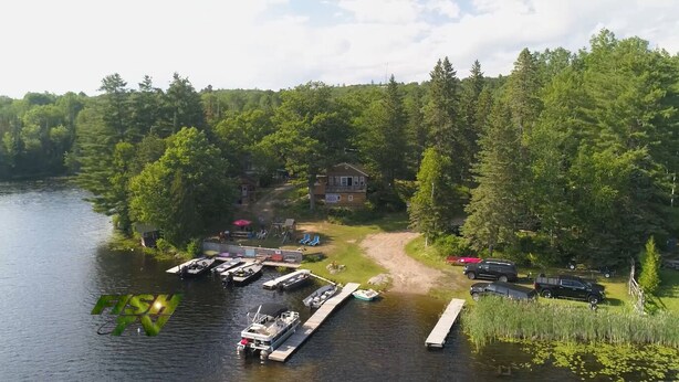 A lakeside property with a dock, boats, and a cabin surrounded by dense forest. - Longmuir's Hidden Cove Cottage Resort (Addington Highlands)
