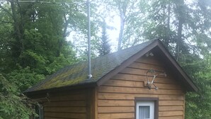 A small wooden cabin with a door and a window, surrounded by greenery. - Longmuir's Hidden Cove Cottage Resort (Addington Highlands)