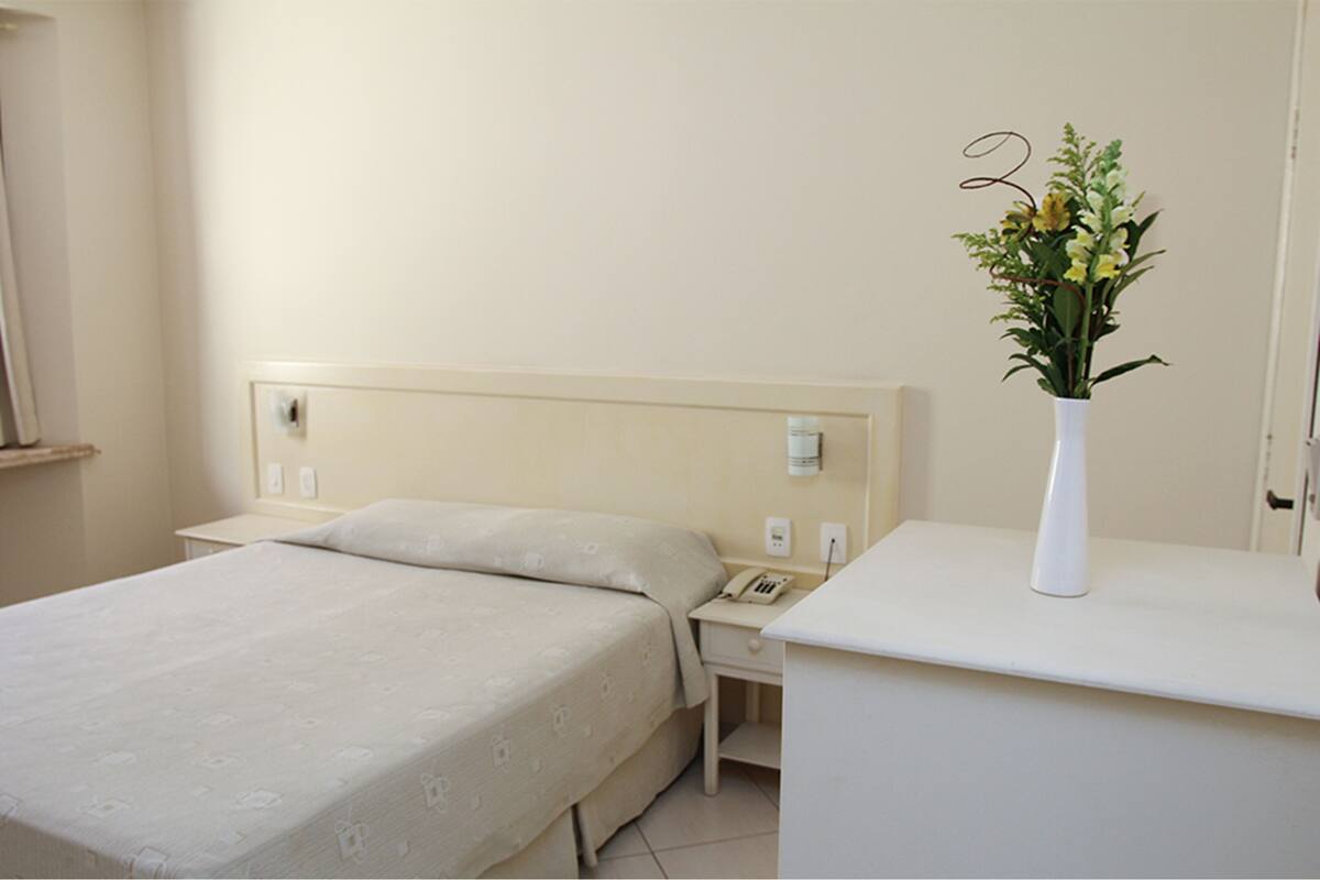 Una habitación de hotel con una cama, mesita de noche y un jarrón con flores.