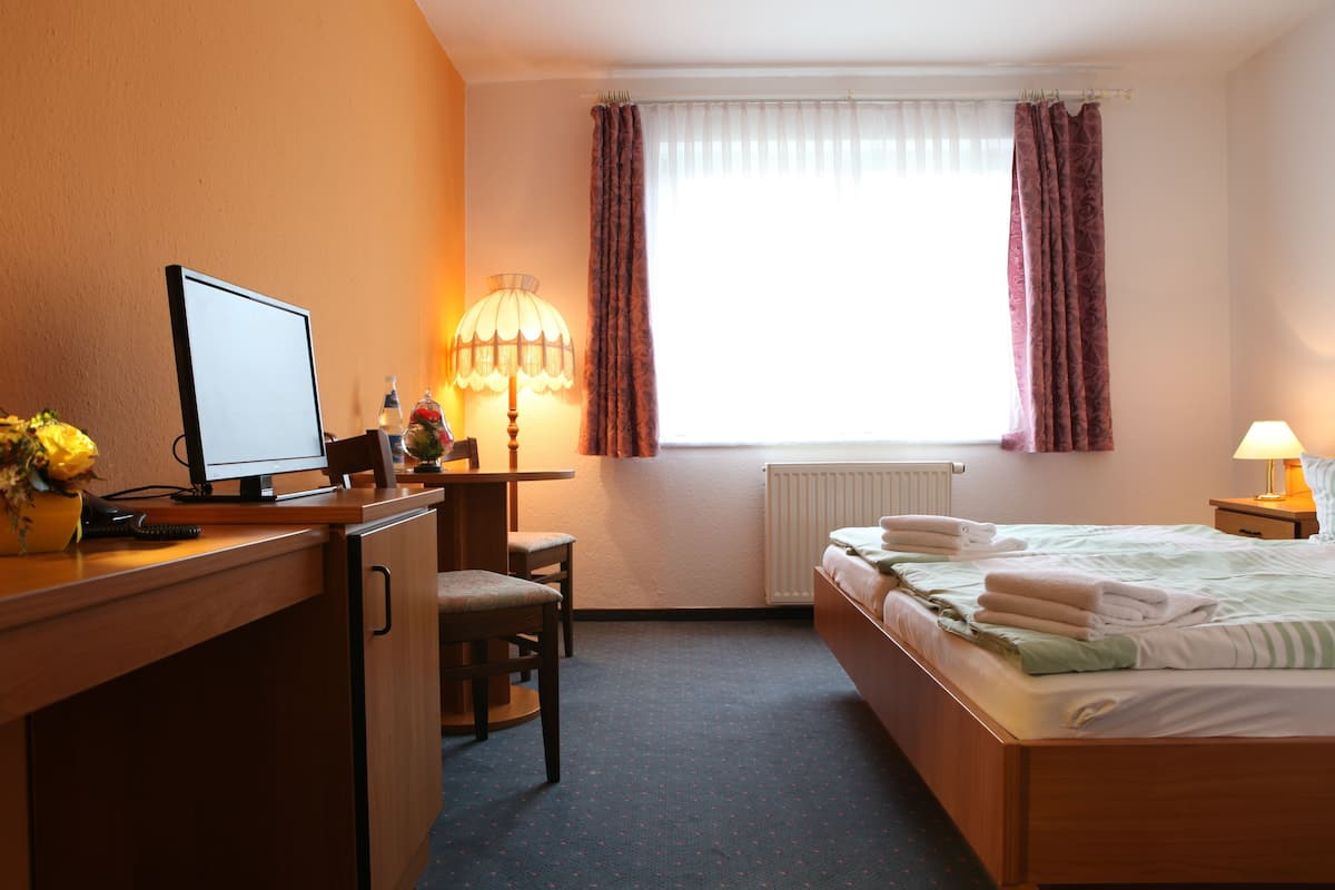 A hotel room with a desk, chair, bed, and a window with curtains.