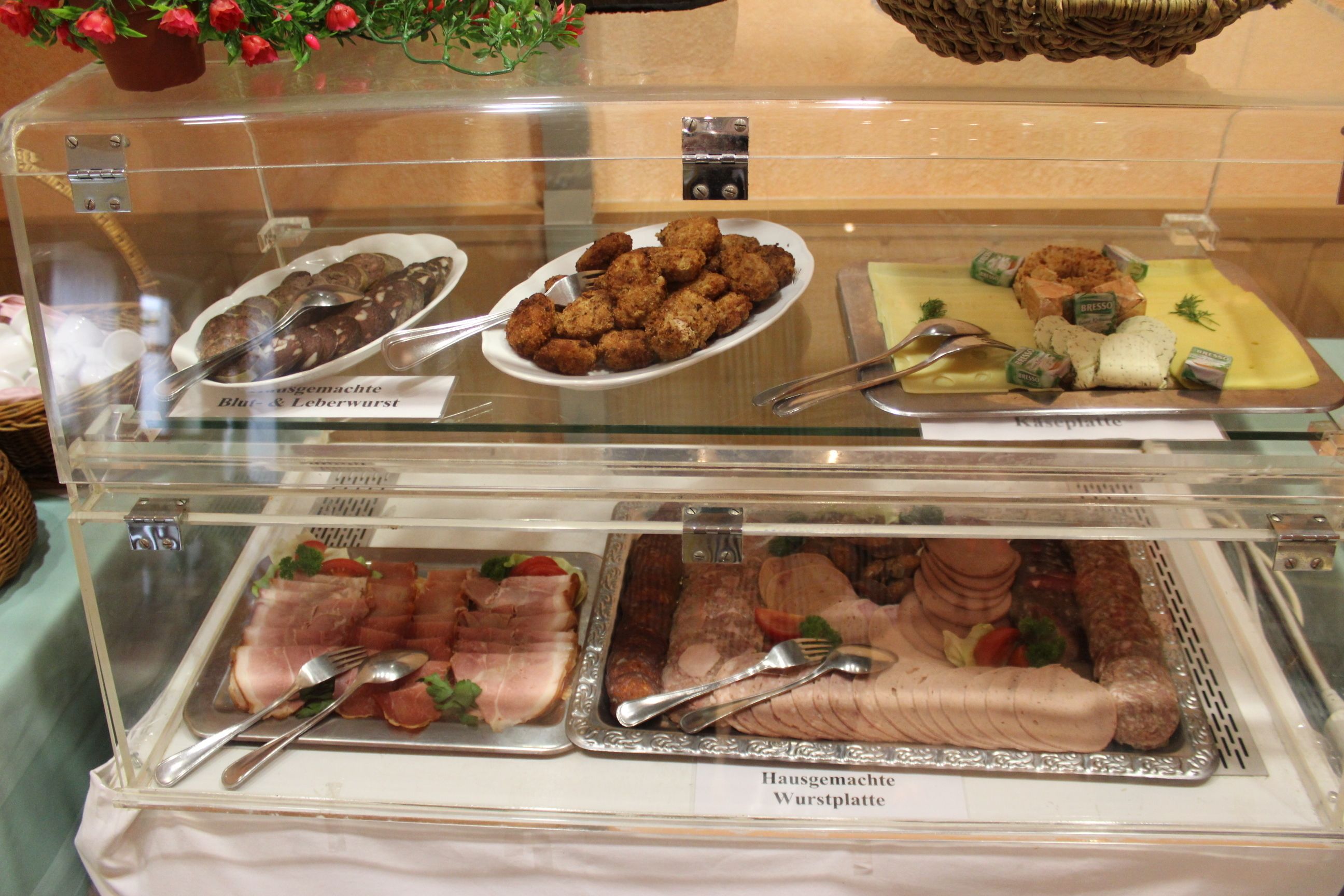 Un buffet proposant divers plats, notamment du saucisson bleu et du saucisson de foie, une assiette de charcuteries et d'autres viandes.