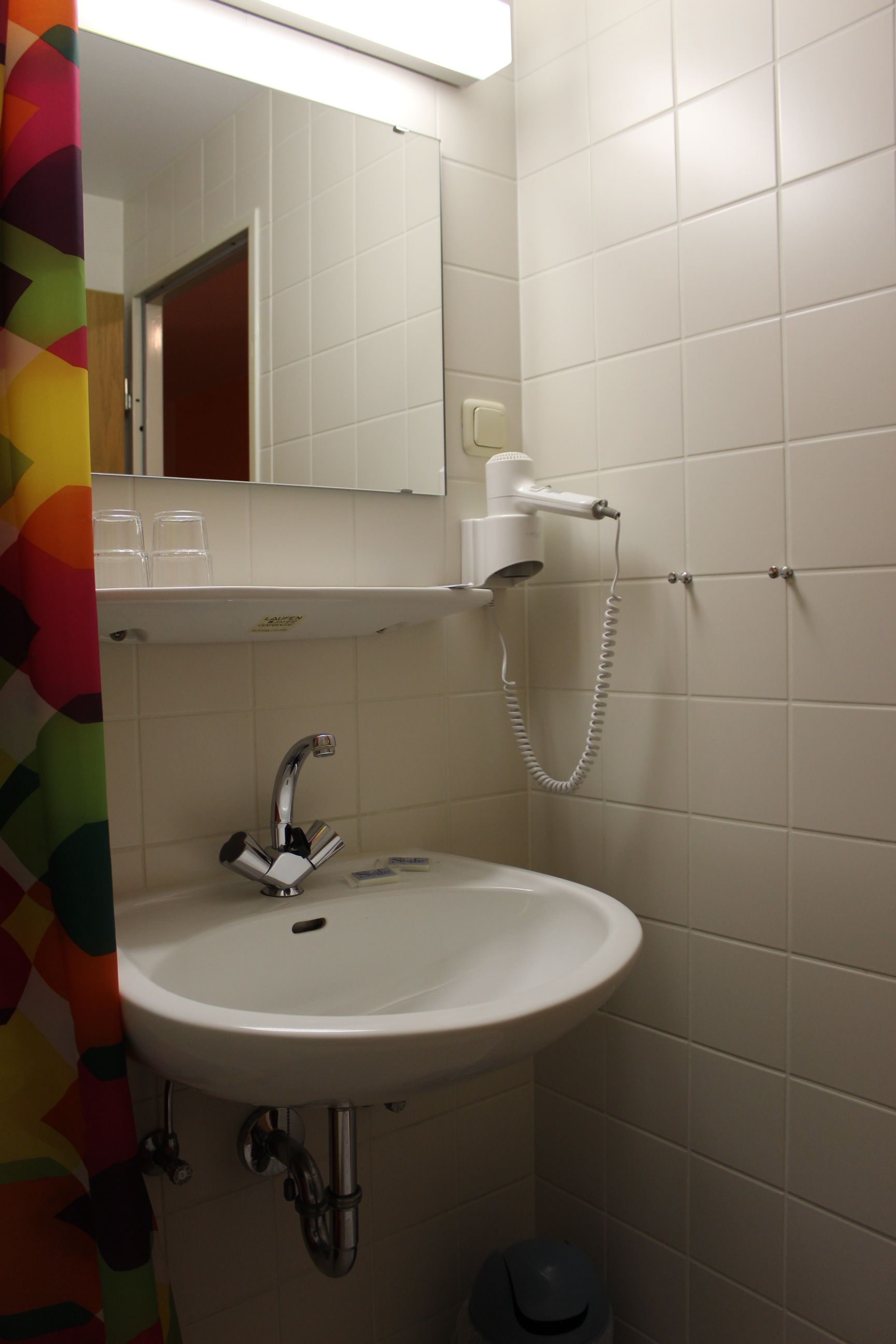 A bathroom with a white sink, a mirror, and a hairdryer on a wall-mounted stand.