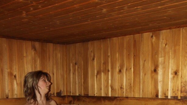 Una persona sentada en un banco de madera dentro de un sauna.