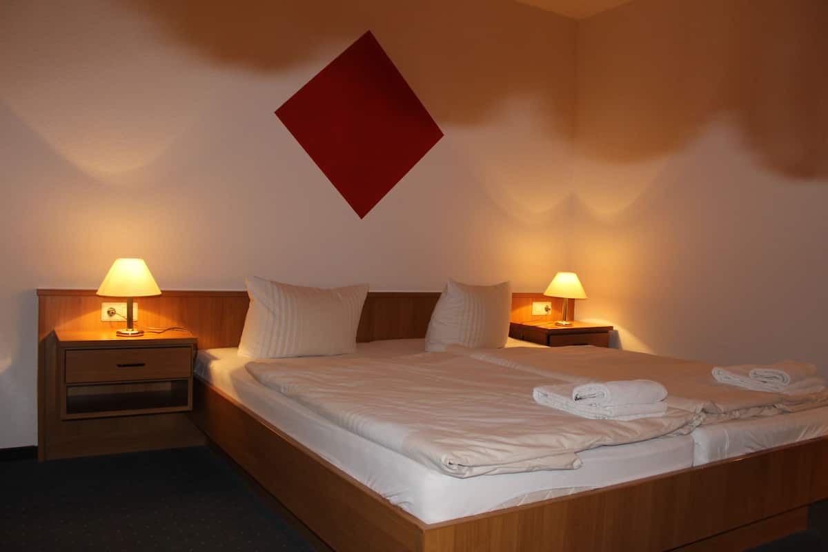 A hotel room with two beds, each with a nightstand and lamp, and a red diamond-shaped decoration on the wall.