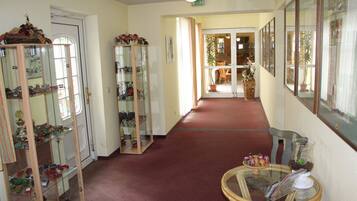 A hallway with glass display cabinets on the left, a glass table with magazines on the right, and a red carpet.