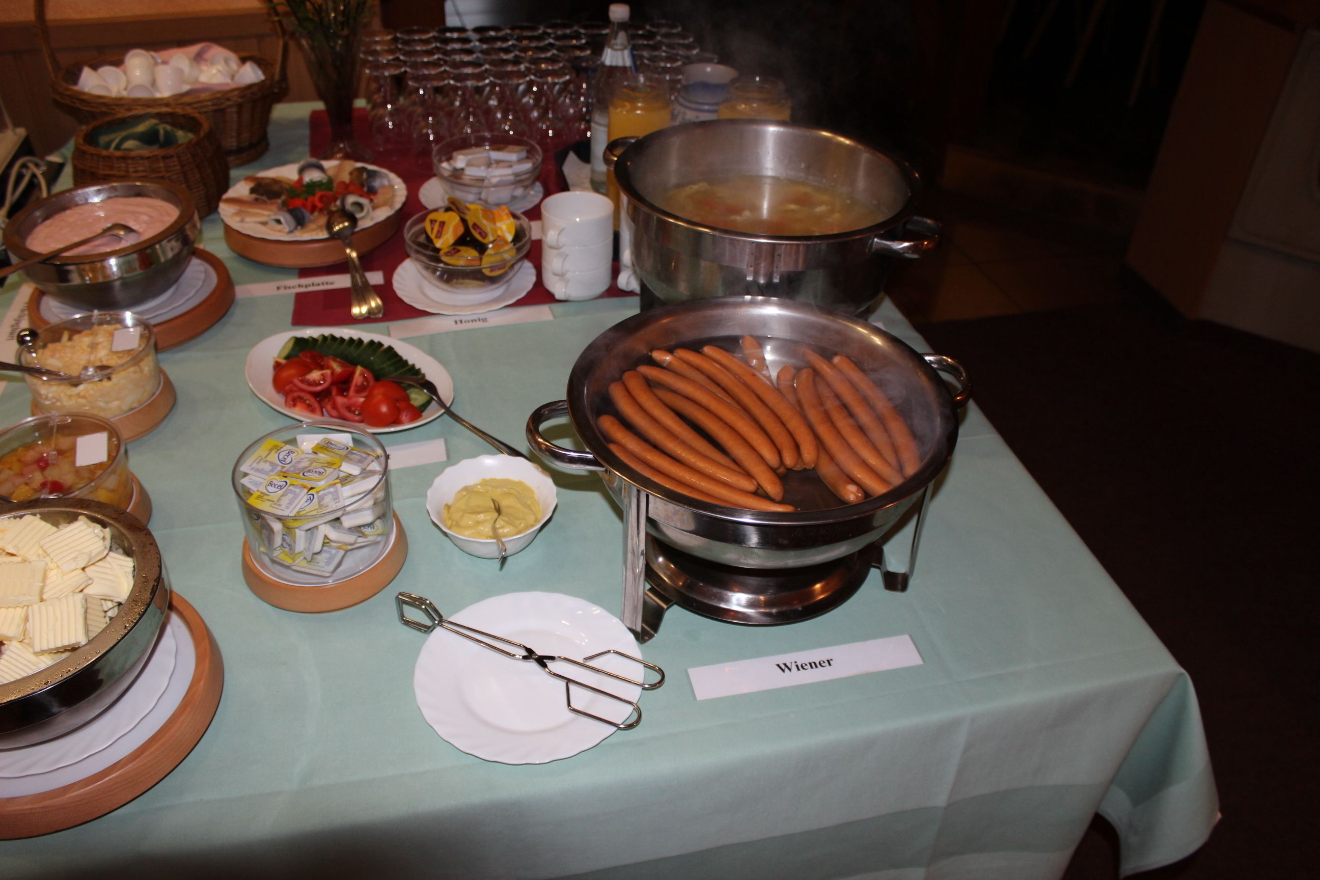 A buffet table with various food items including a pot of hot dogs, bowls of soup, and plates of vegetables.