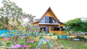 A two-story house with a balcony, surrounded by lush greenery and flowering plants. - Beautiful View Lodging (San Andrés)