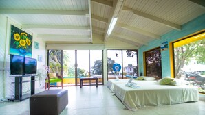 A spacious room with a bed, a TV, and a large window offering a view of the outdoors. - Beautiful View Lodging (San Andrés)