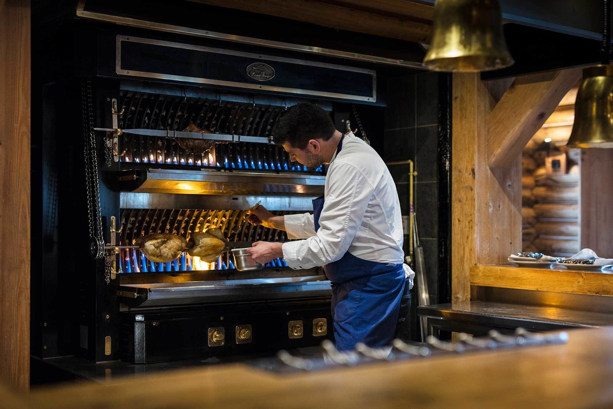 Um chef preparando comida em uma cozinha profissional, equipada com um forno grande e superfícies de aço inoxidável.