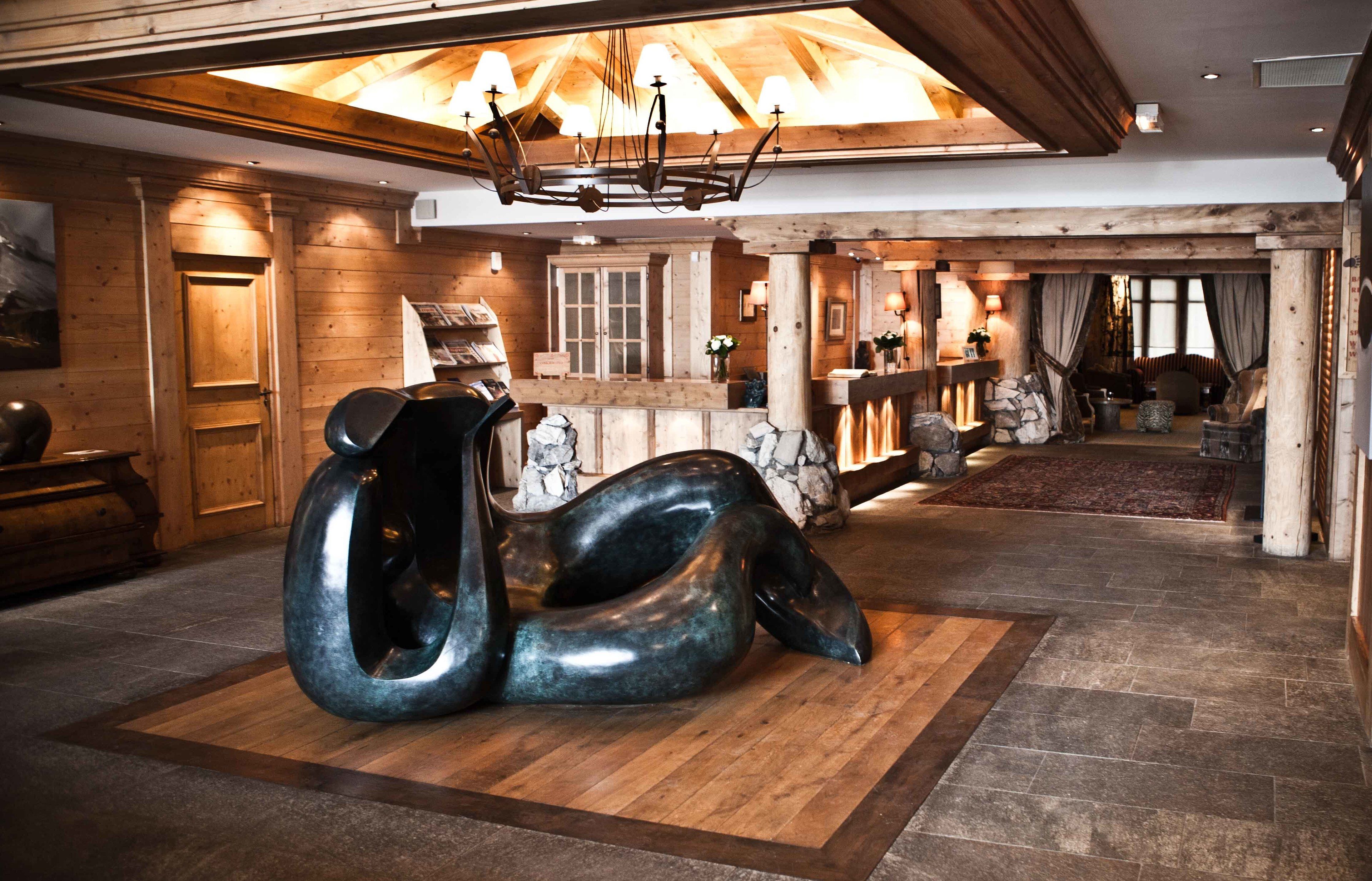 Un vestíbulo amplio con una gran escultura abstracta, vigas de madera y un candelabro.