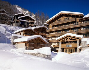 A multi-story wooden lodge with balconies, stone walls, and snow-covered roofs.