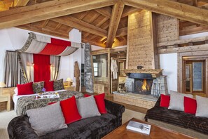 A spacious living area with a fireplace, a large bed with red and grey bedding, and a cozy seating area with red and grey cushions.