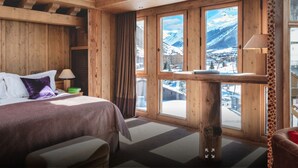Una stanza in legno con un letto, un tavolo e vista su un paesaggio montano innevato.