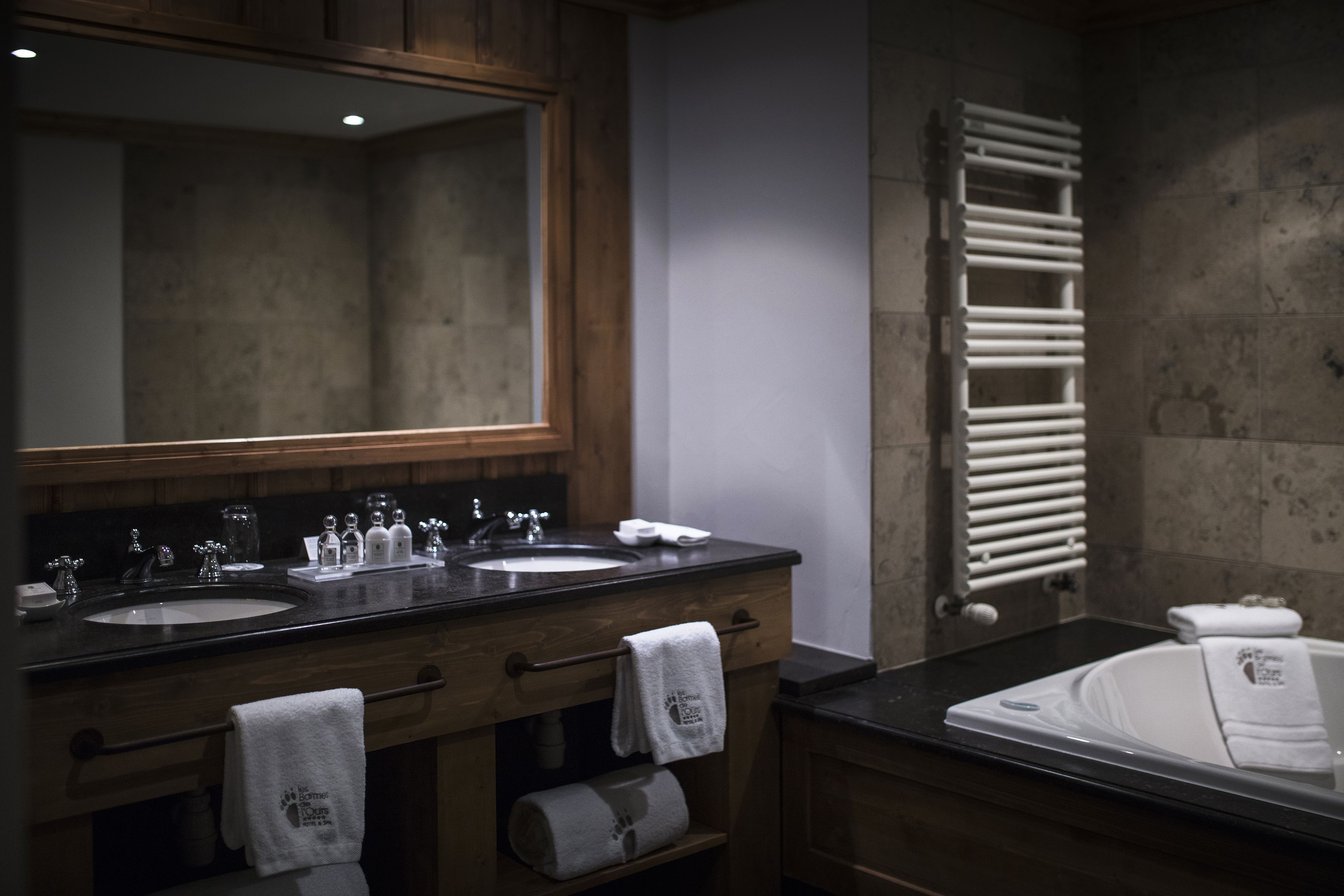 A bathroom with two sinks, a large mirror, a towel rack, and a bathtub.