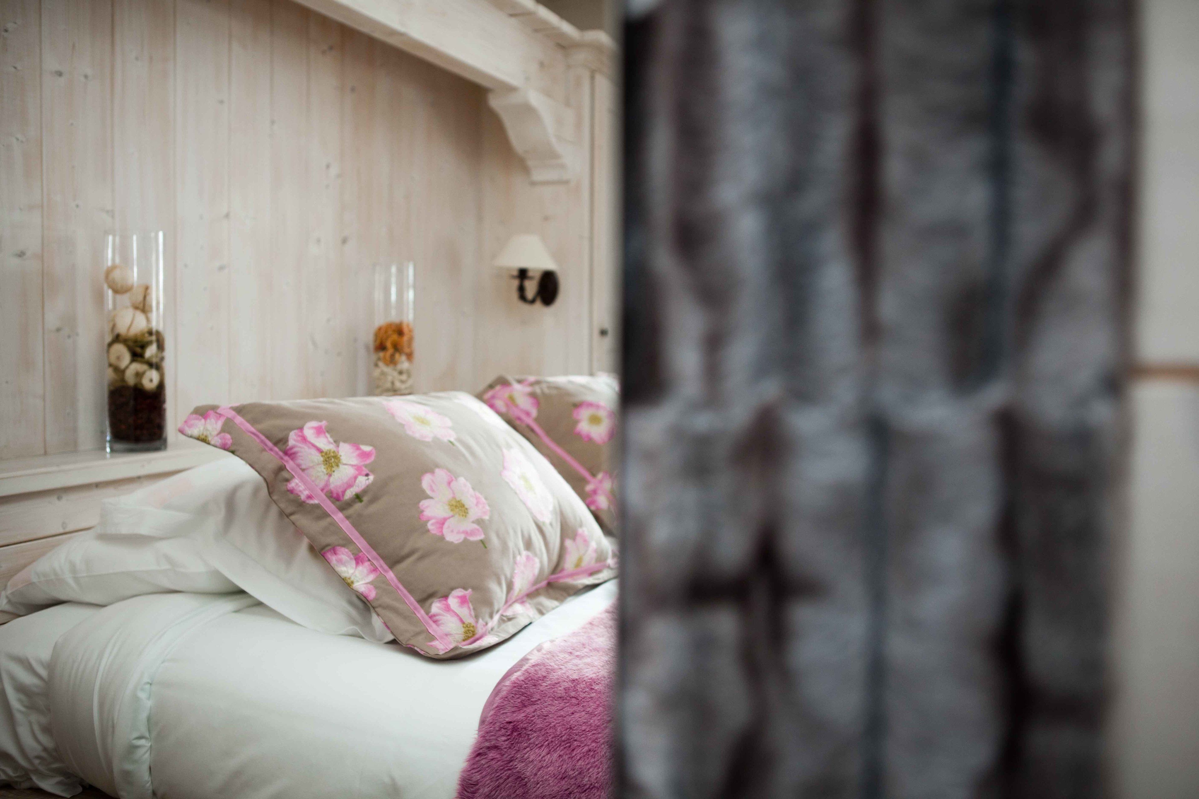 Ein Schlafzimmer mit einem Holzkopfende, floraler Bettwäsche und einer Vase mit getrockneten Blumen auf dem Nachttisch.