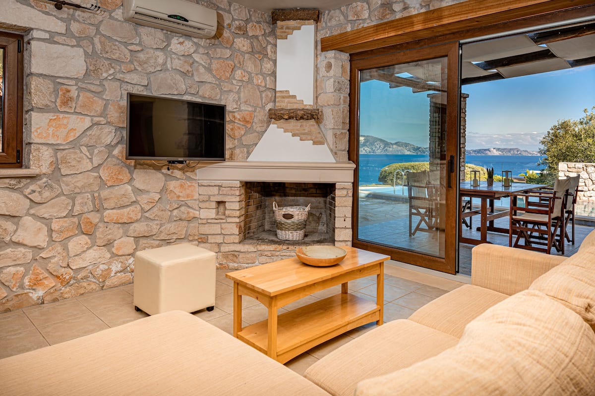 Una habitación de paredes de piedra con chimenea, televisión y vistas al mar.