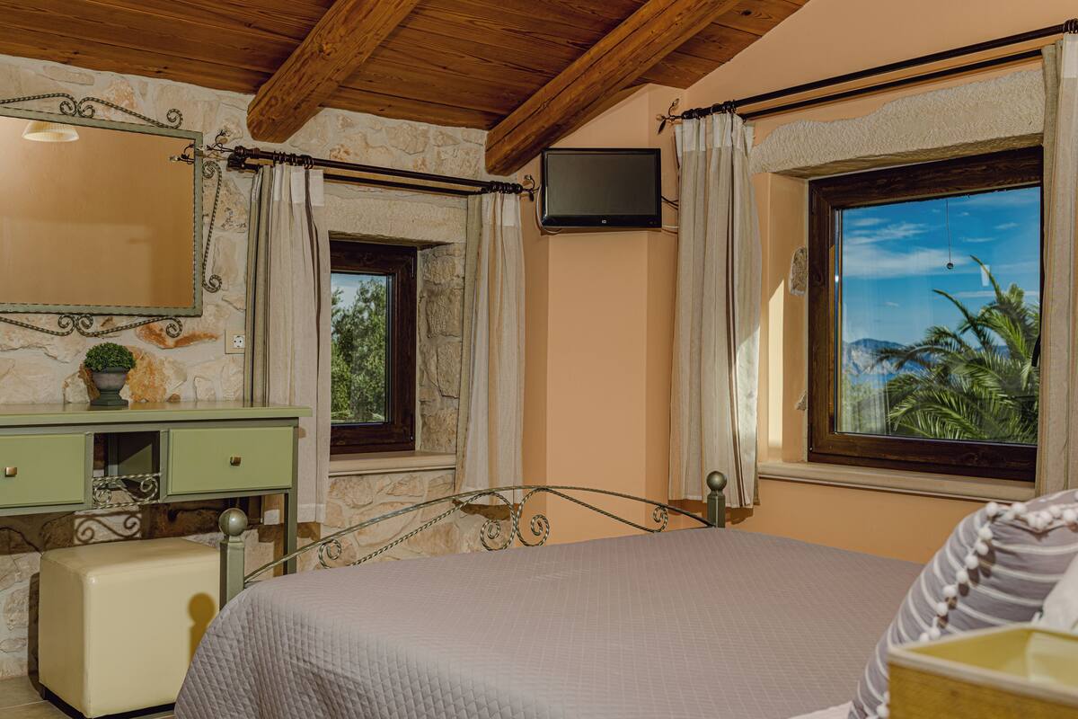 Un dormitorio con cama, cómoda, televisor y ventanas con cortinas.