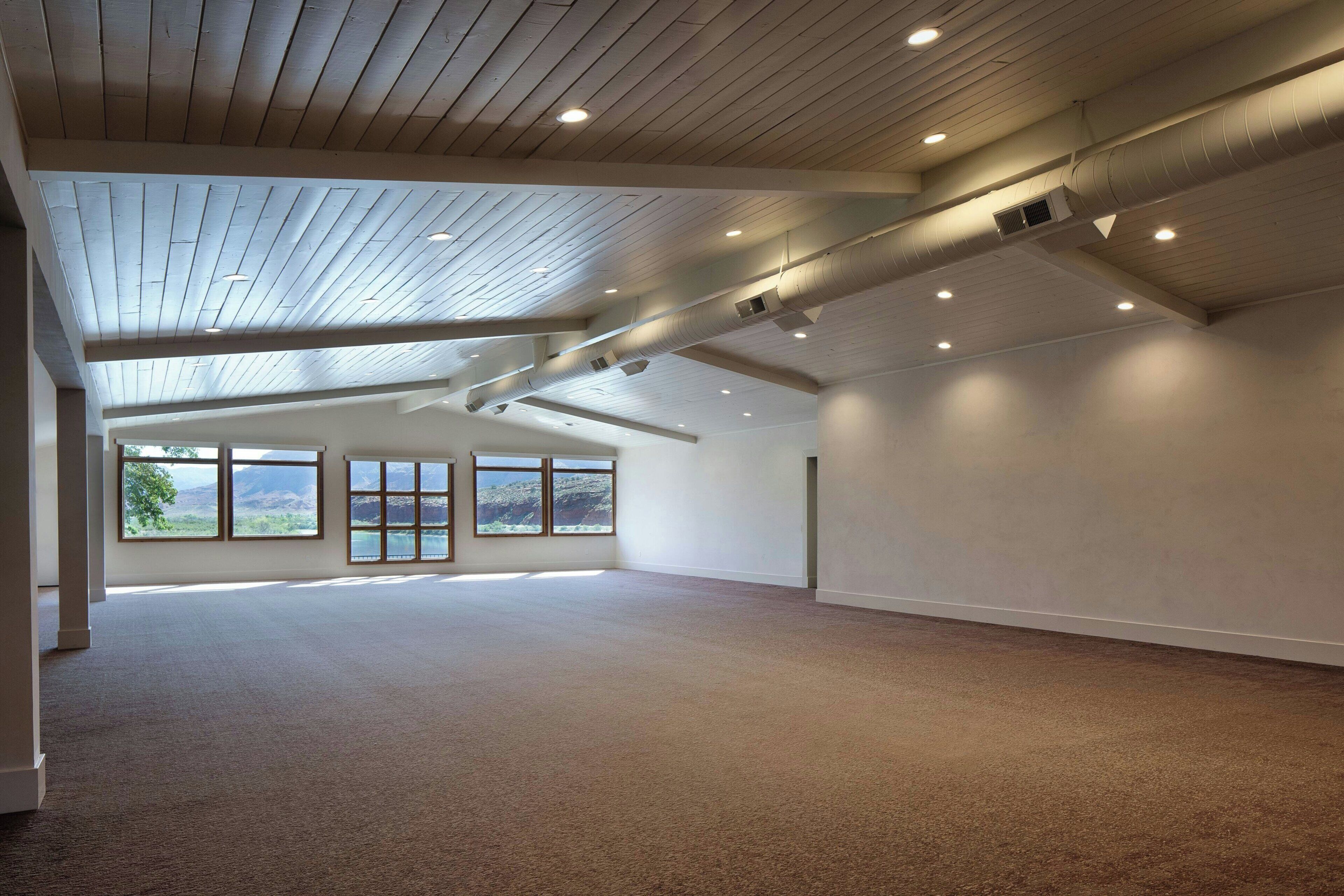 Een ruime kamer met een hoge plafond, grote ramen en een vloerbedekt met tapijt.