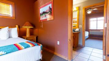 A bedroom with a bed, a nightstand, a lamp, a painting, and a door leading to another room.