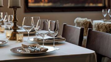 A dining table set with plates, glasses, and cutlery, with a candle holder and a view of a mountainous landscape through a window.