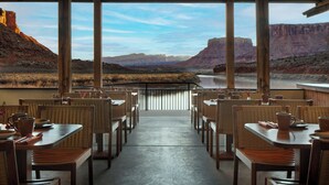 Un espace extérieur aménagé pour les repas, avec des tables et des chaises, offrant une vue sur un canyon et une rivière.