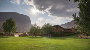 Une vaste étendue d’herbe, un espace dégagé, avec un bâtiment en bois doté d’un balcon et offrant une vue sur une montagne.