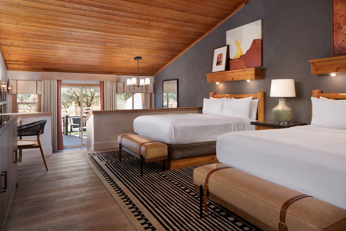 A hotel room with two beds, a desk, and a view of the outdoors.
