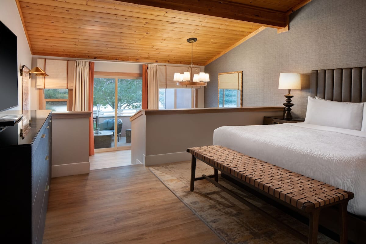 A bedroom with a large bed, wooden bench, and a view of the outdoors.