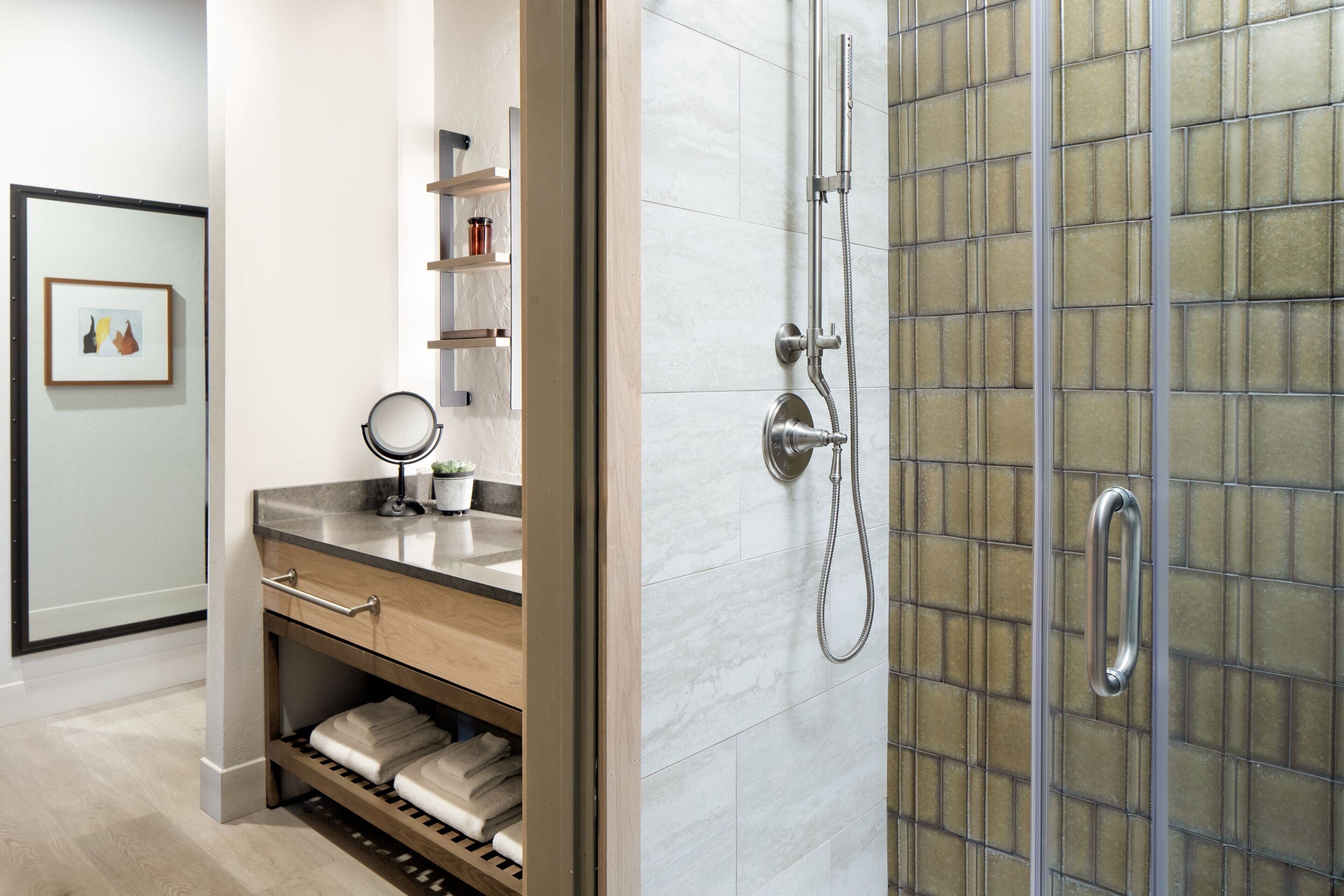 A modern bathroom with a wooden vanity, a glass shower enclosure, and a framed picture on the wall.
