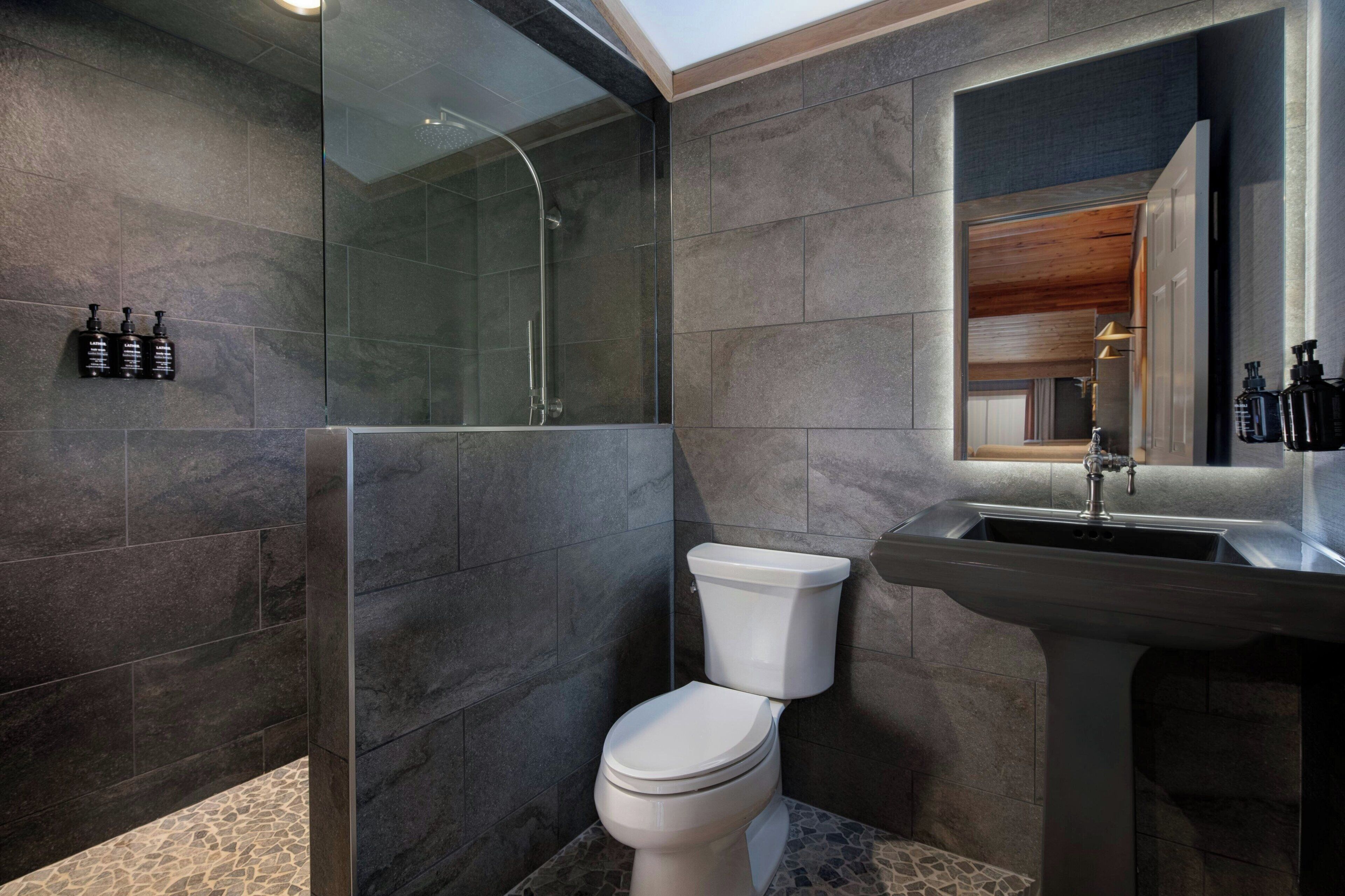 Un baño moderno con ducha de vidrio, inodoro blanco y lavamanos con espejo.